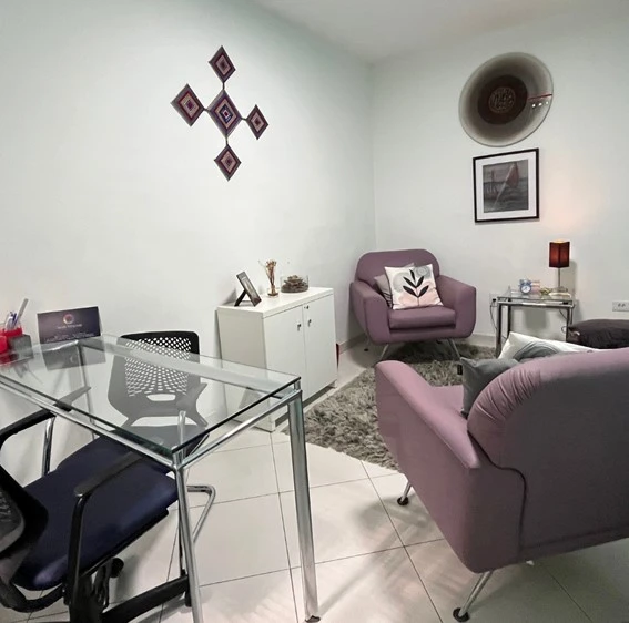 Consultório humanizado na Saúde Integrada com poltronas roxas acolhedoras, mesa de vidro e design baseado em neuroarquitetura para psicólogos e médicos.